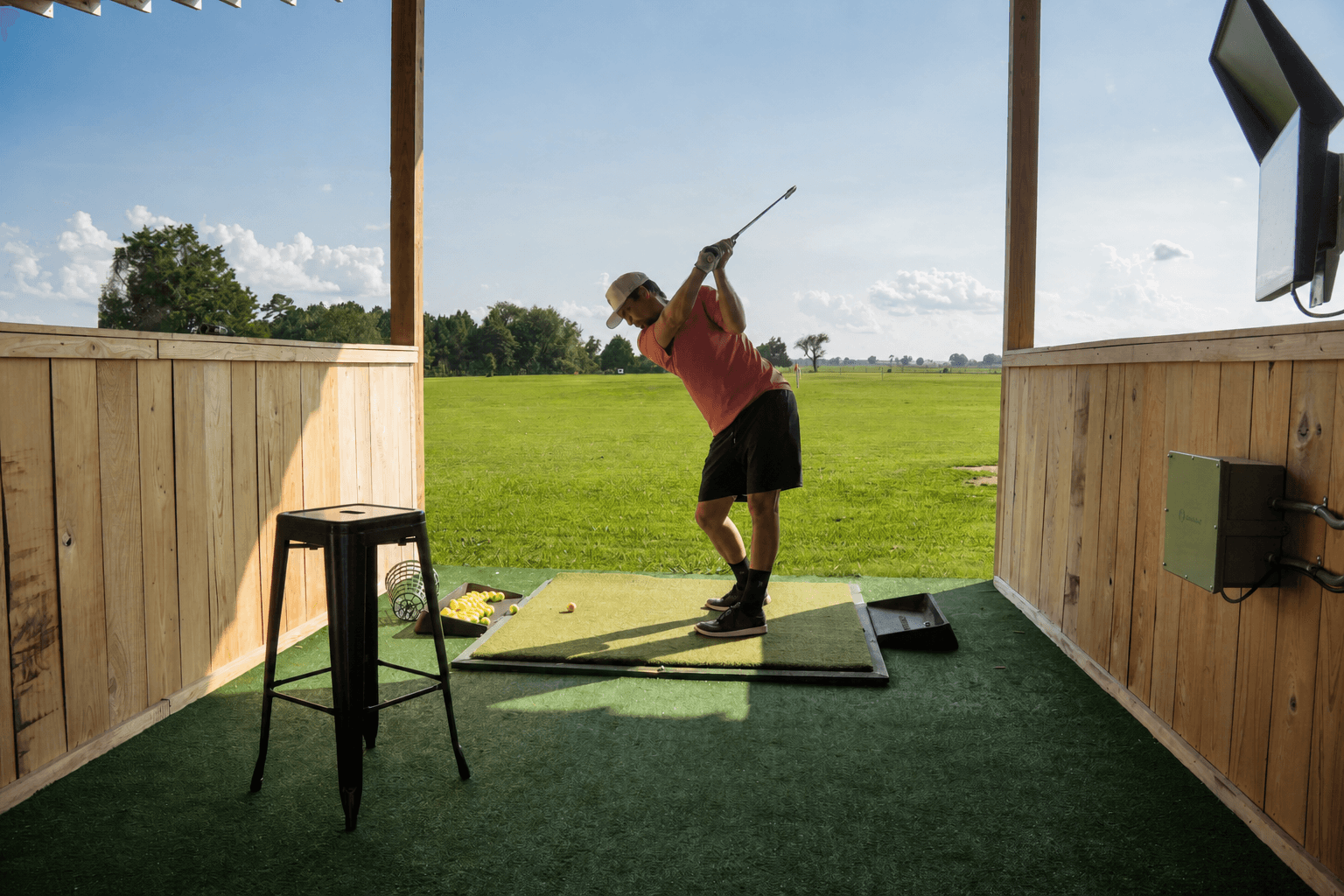 Golfer swinging at Toptracer bay with screen visible and range behind